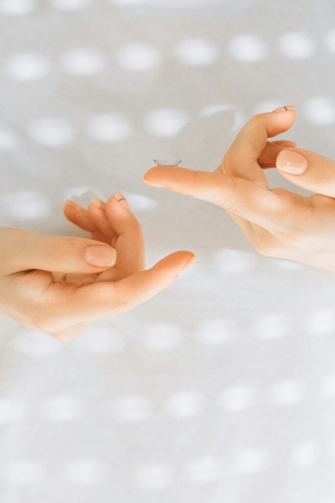 A detailed close-up of hands carefully handling a contact lens against a softly lit background.